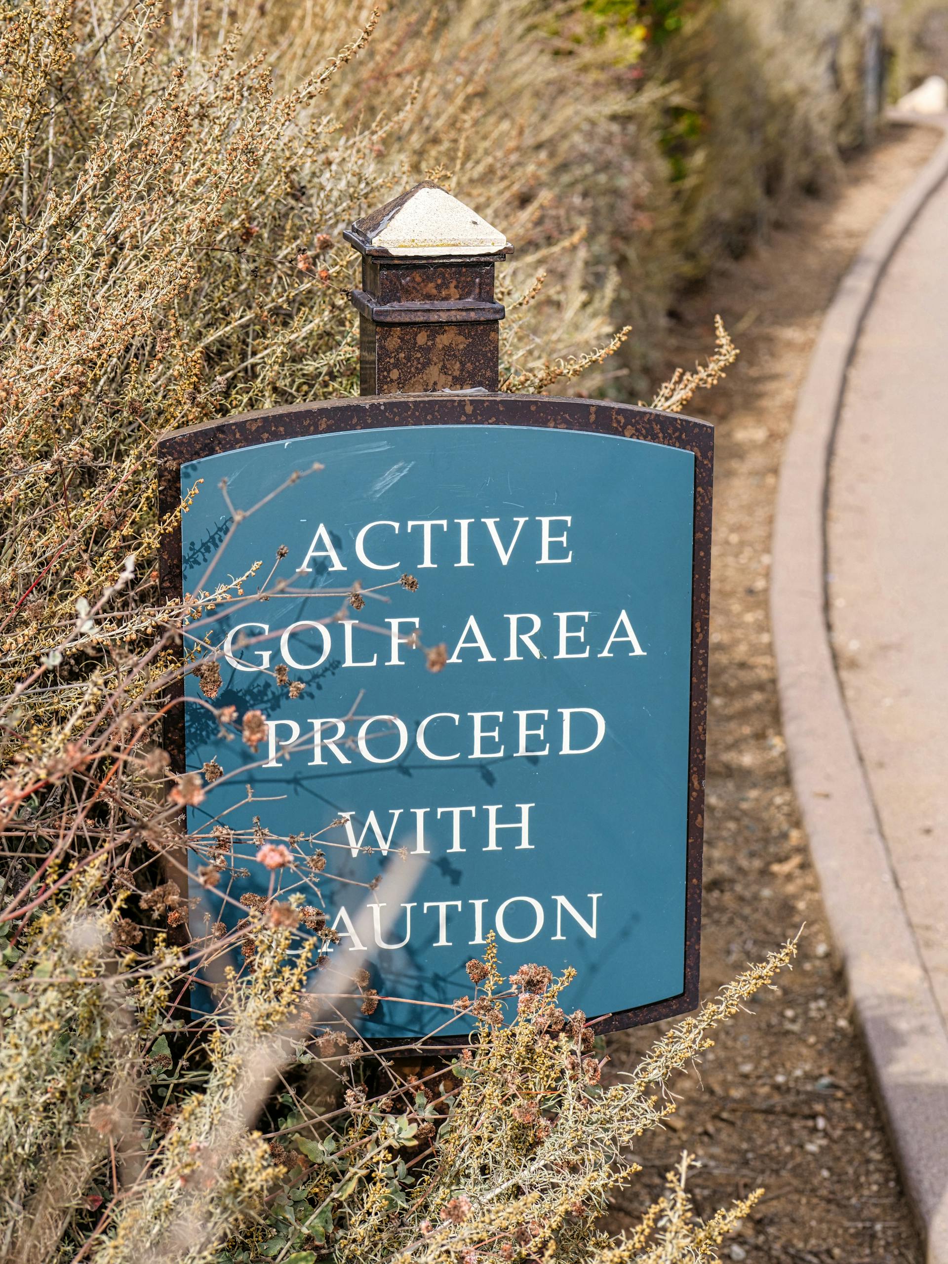 Sign in a golf park warns to proceed with caution, surrounded by foliage.